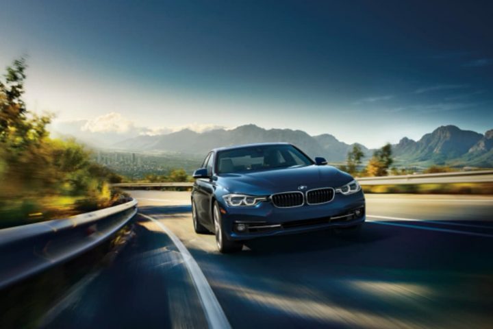 A BMW 330i driving on a highway with mountains in the background.