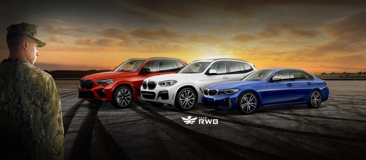 A uniformed American service member looks at red white and blue BMWs parked on rubber marked tarmac