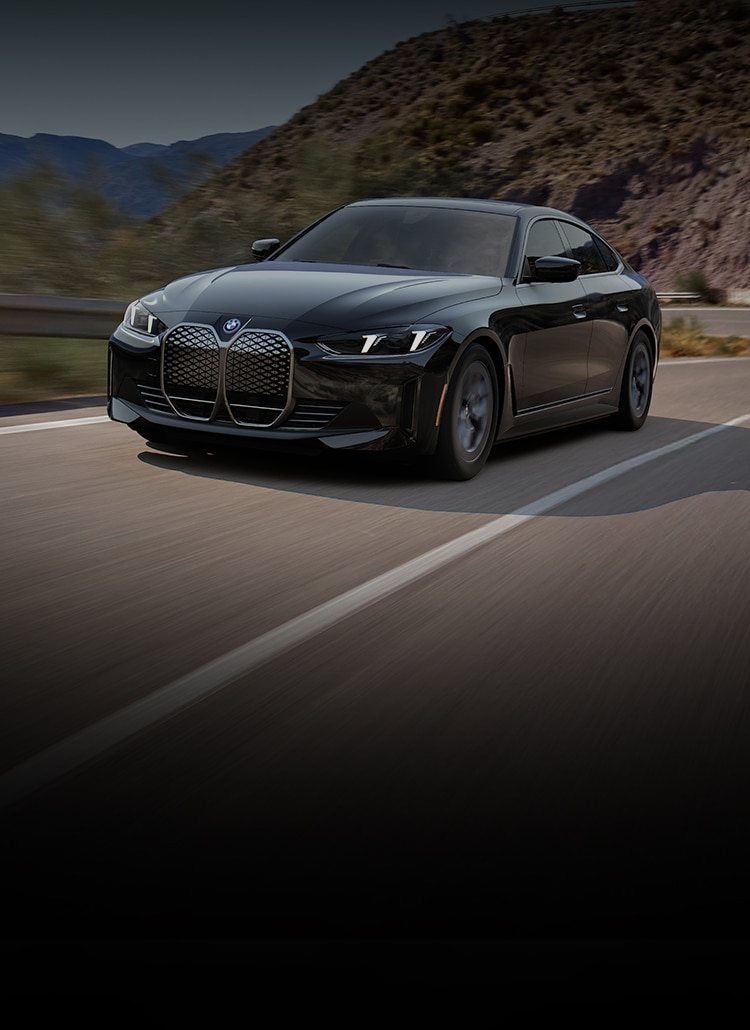 The 2025 BMW i4 eDrive40 winding around a rural highway with a mountain landscape in the background.