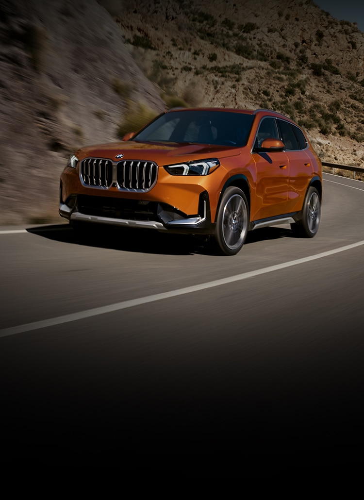 The 2025 BMW X1 xDrive28i winding around a rural highway with blurred mountains in the background.