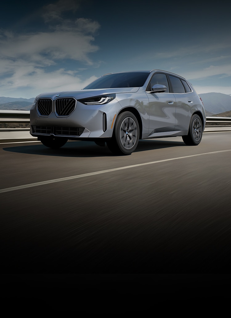 The 2025 BMW X3 30 xDrive speeding down a highway with a bright blue sky in the background.