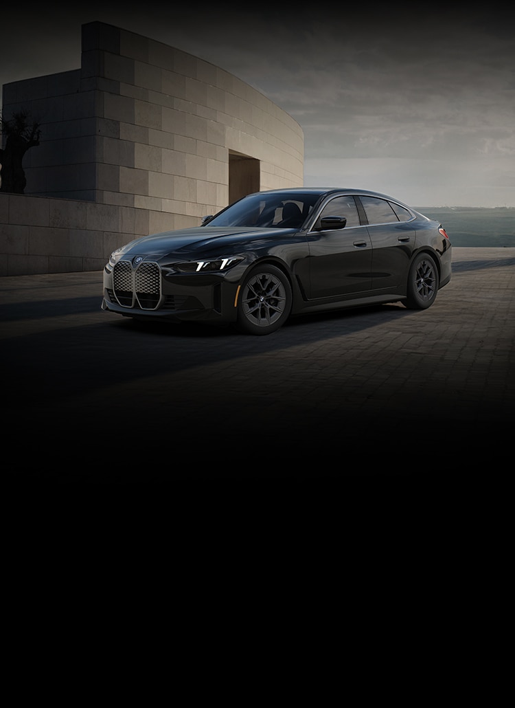 The 2025 BMW i4 eDrive40 parked at a modern industrial building by the sea. 