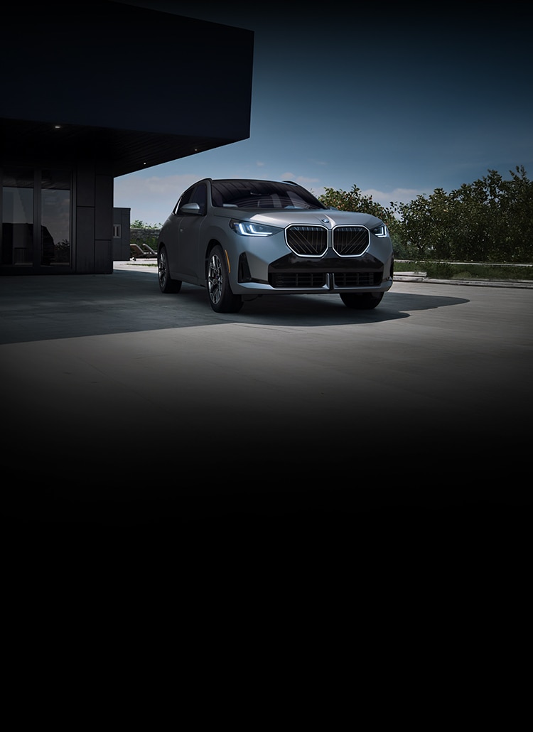 A BMW X3 sits parked outside a modern home on a sunny day.