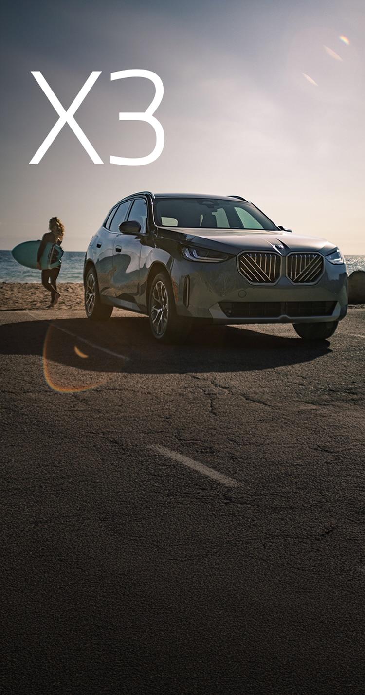 The BMW X3 30 xDrive parked on a beachfront with a surfer walking away from it toward the ocean.