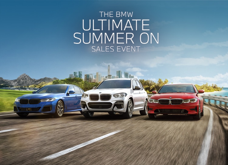 Red, white, and blue BMW vehicles drive together along a seaside highway.