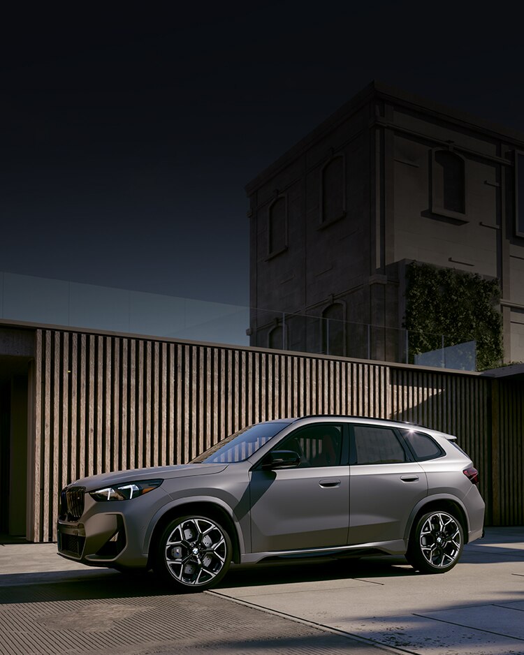 Side view of the BMW X1 SUV parked in front of wooden structure