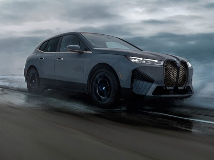 The BMW iX M60 SUV driving through saltwater against a moody cloudy background