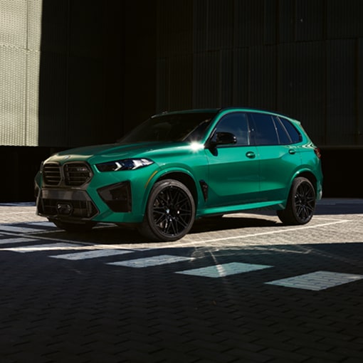 A 2025 BMW X5 M Competition SUV waiting at a crosswalk