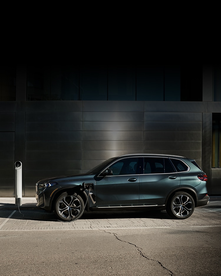 2025 BMW X5 xDrive50e charging in front of a shiny metal building