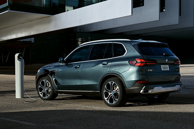 Rear quarter shot of the 2025 BMW X5 xDrive50e PHEV parked beside a charging station