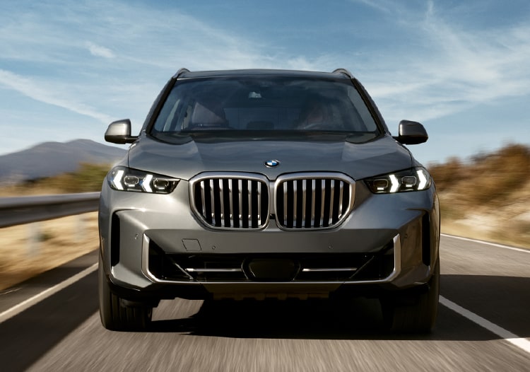 Front view of a 2025 BMW X5 speeding down a desert road