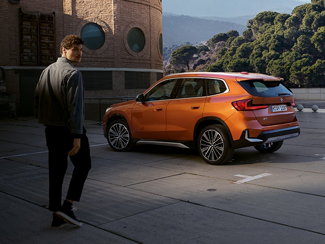 A man walks towards a parked 2023 BMW X1 SAV in Utah Orange Metallic