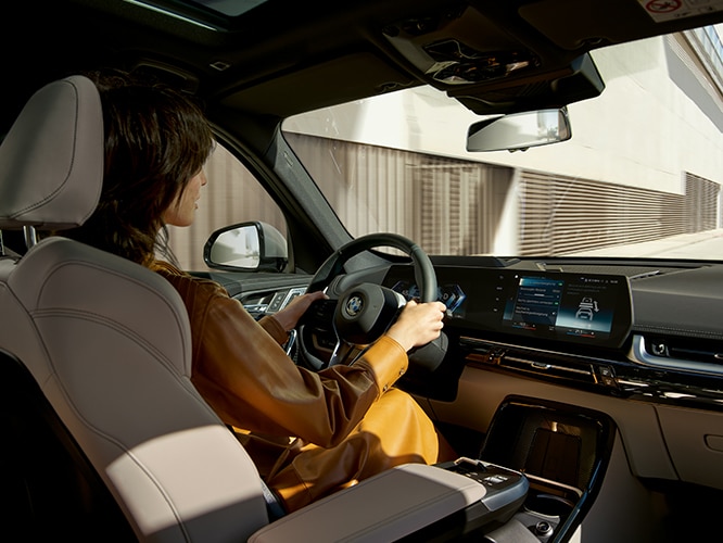 A woman confidently drives the 2023 BMW X1 SAV with extended safety systems standard