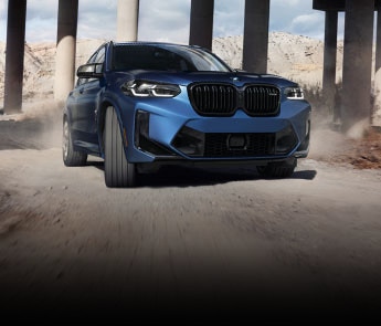 The 2022 BMW X3 M drives on a rugged twisting road beneath an overpass