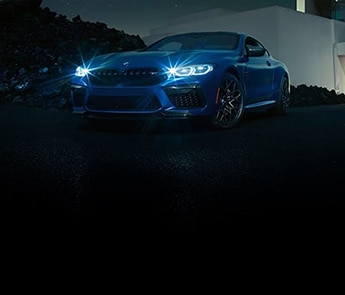 An exterior view of the M8 Coupe parked outside a modern luxury home