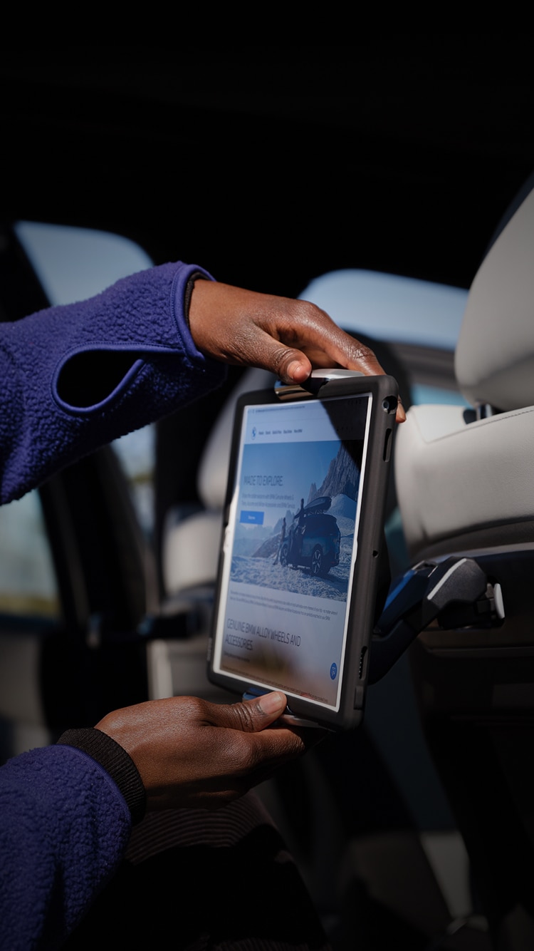 Detail of a boy's hand adjusting the Available Tablet Holder for BMW Travel and Comfort System in the backseat of a BMW SUV