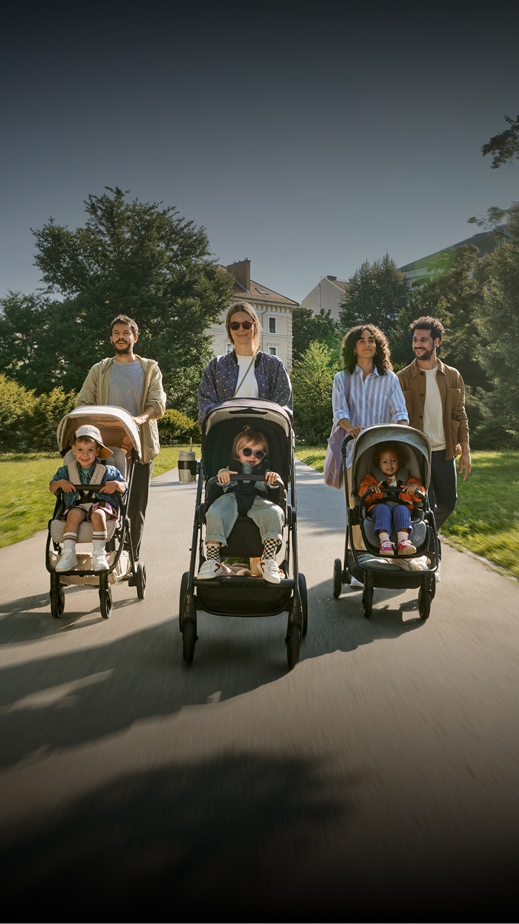 Confident parents push their young children in Nuna strollers through a park on a sunny day