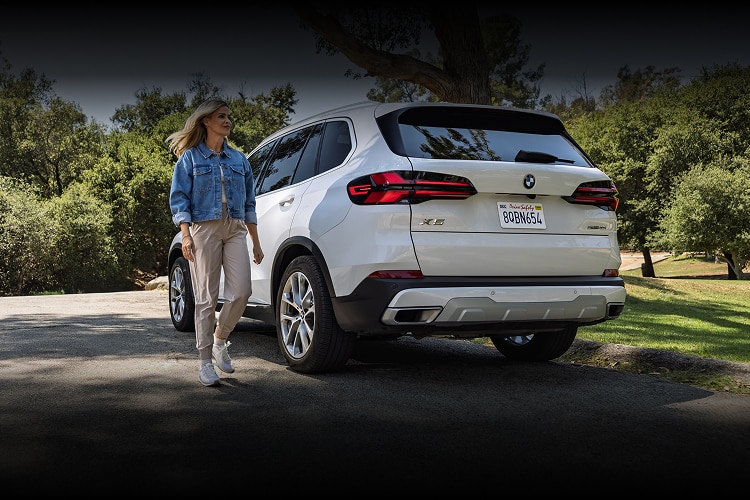 A woman smiles as she exits her parked BMW X5 SUV at a park