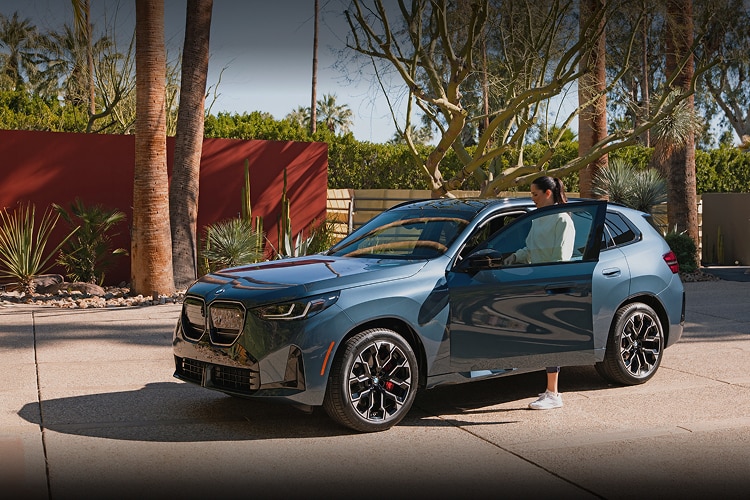 Ana Ivanović gets into a BMW X3 M50 xDrive, which is parked in a desert driveway on a sunny day