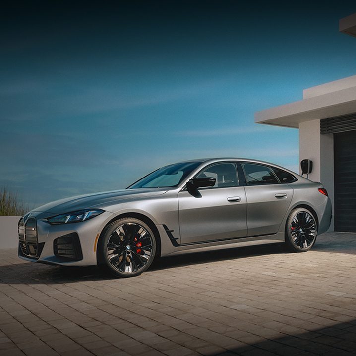 A BMW i4 parked in a driveway overlooking a large body of water.