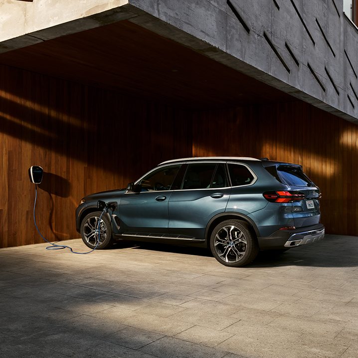 A BMW X5 plugged into a BMW Wallbox in a large wood-paneled garage.