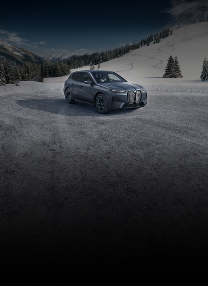 A BMW iX parked on a snow-covered road amidst a snowy mountain environment.