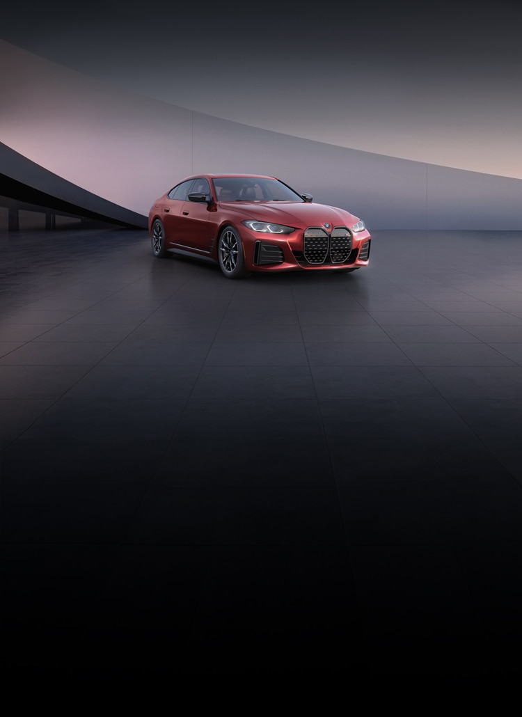A BMW i4 M50 parked on a tile surface in front of a dramatically lit modern white structure.