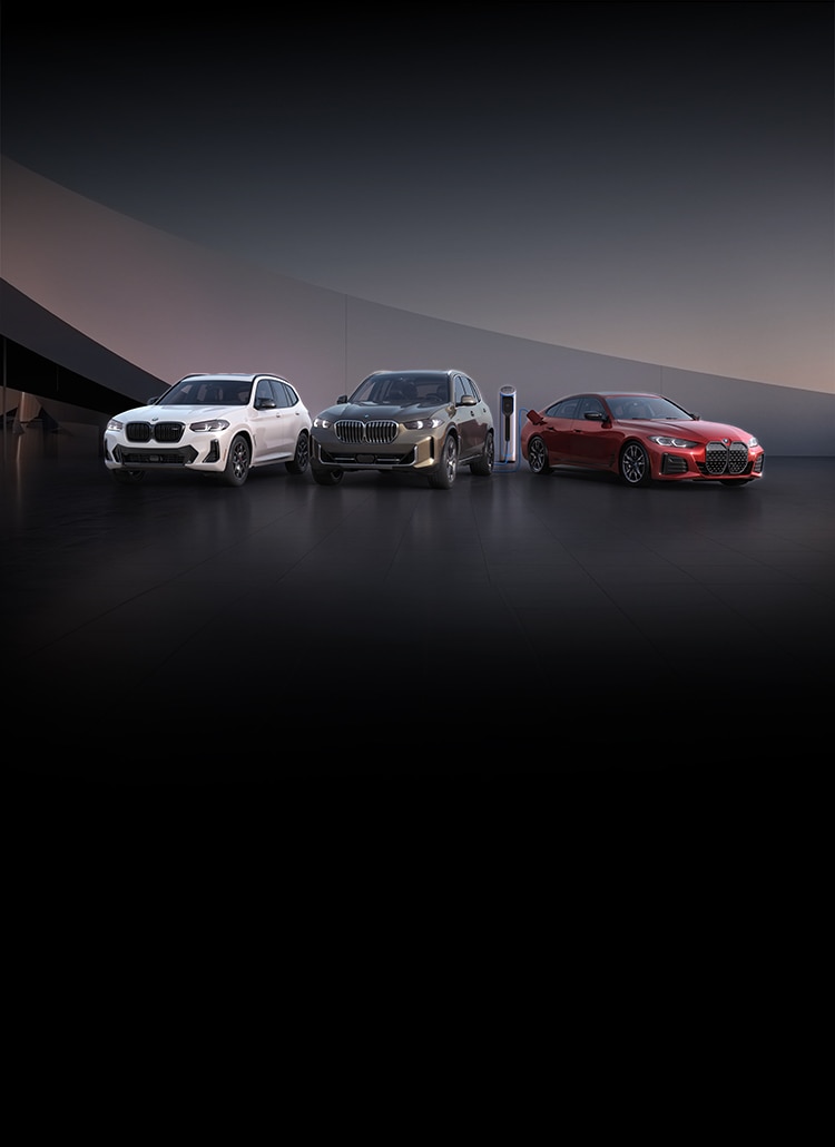 The BMW X3, X5, and i4 side-by-side in a modern, abstract landscape, with the i4 plugged into an EV charging station.