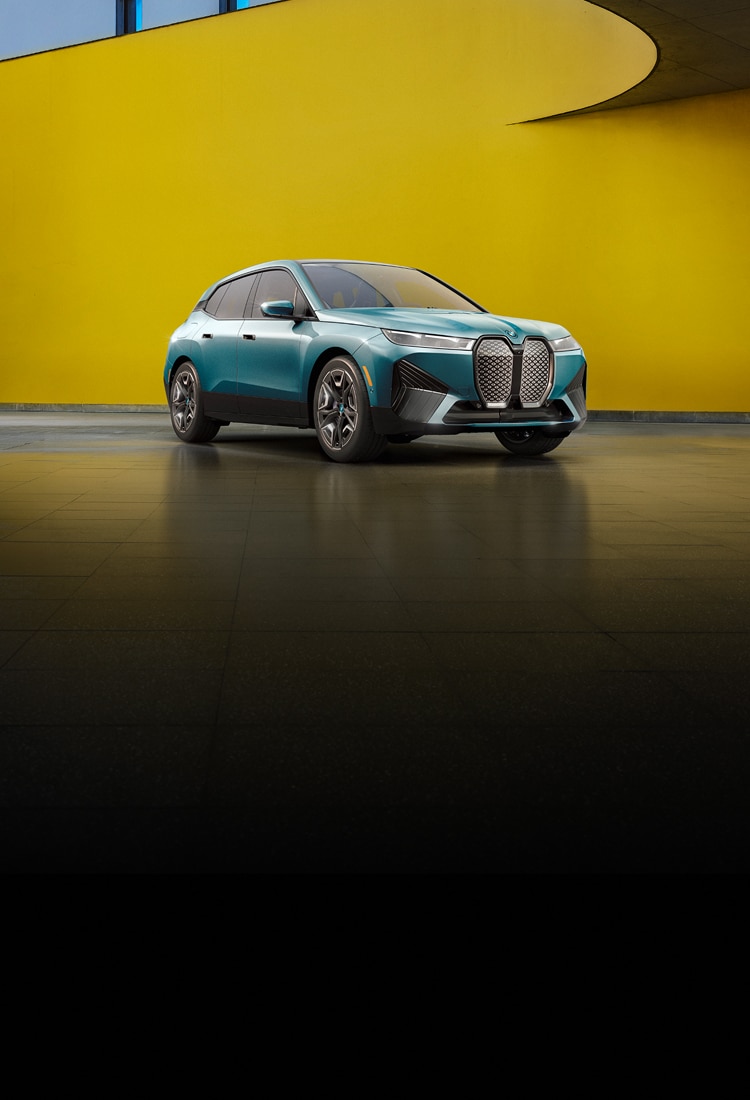 Angled view of a parked BMW iX xDrive50 in a sleek space with a curved yellow wall.