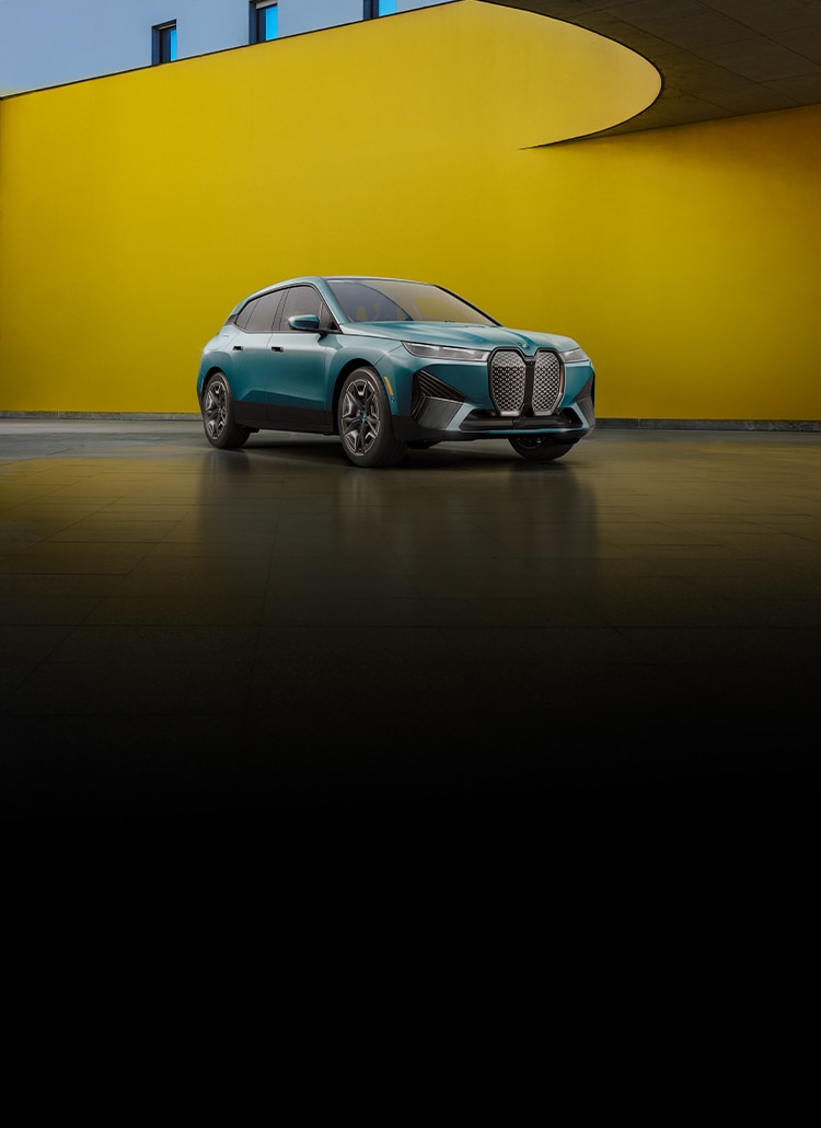 Angled view of a parked BMW iX xDrive50 in a sleek space with a curved yellow wall.