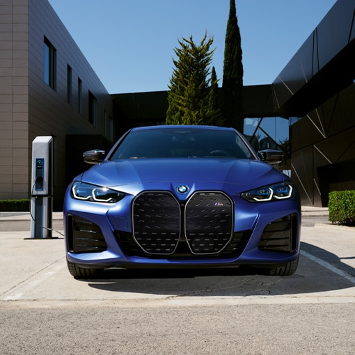 A 2022 BMW i4 M50 parked in front of a modern building, plugged into a public charging station 