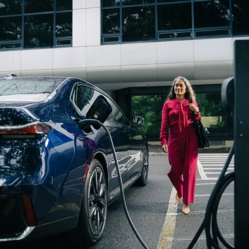 A BMW owner approaches her BMW EV which is plugged into a public charging station