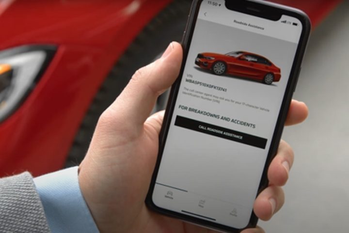 Image of a BMW owner holding their smartphone, showing the BMW Roadside Assistance feature