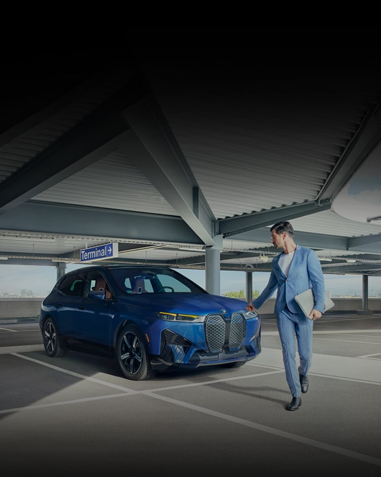 A sharply-dressed man walks away from a parked BMW iX xDrive50 in a parking garage