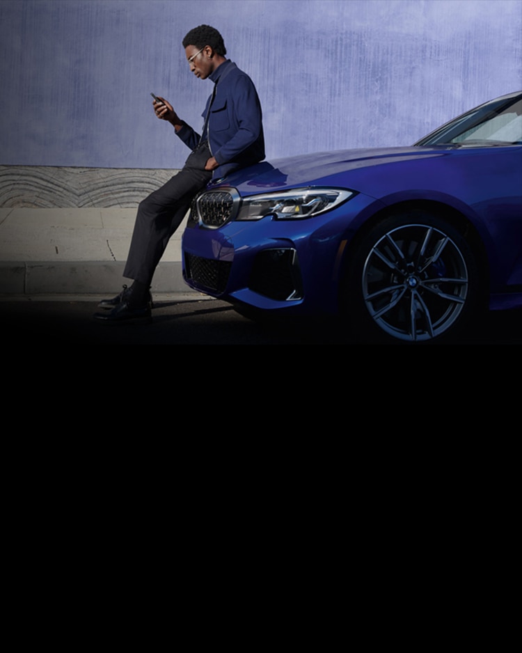 A BMW owner sits on the hood of his vibrant blue BMW