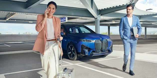 A couple in business attire walk away from their BMW in a parking garage