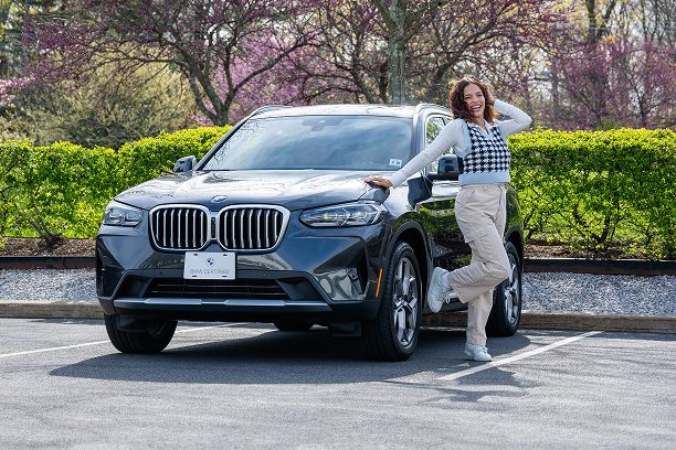 A happy new grad poses next to her BMW