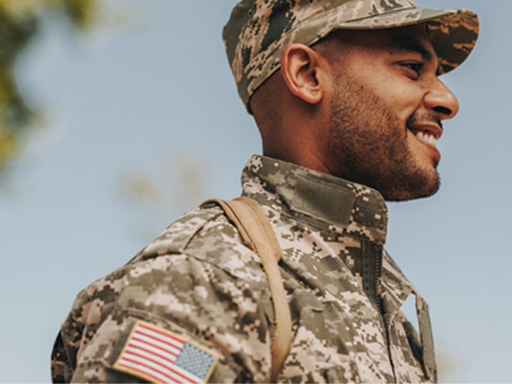 A smiling military member in uniform stands in front of a clear sky
