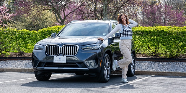 A happy new grad poses next to her BMW