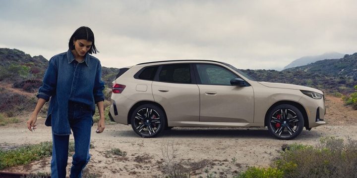 A woman walks away from her parked BMW in a mountainous landscape