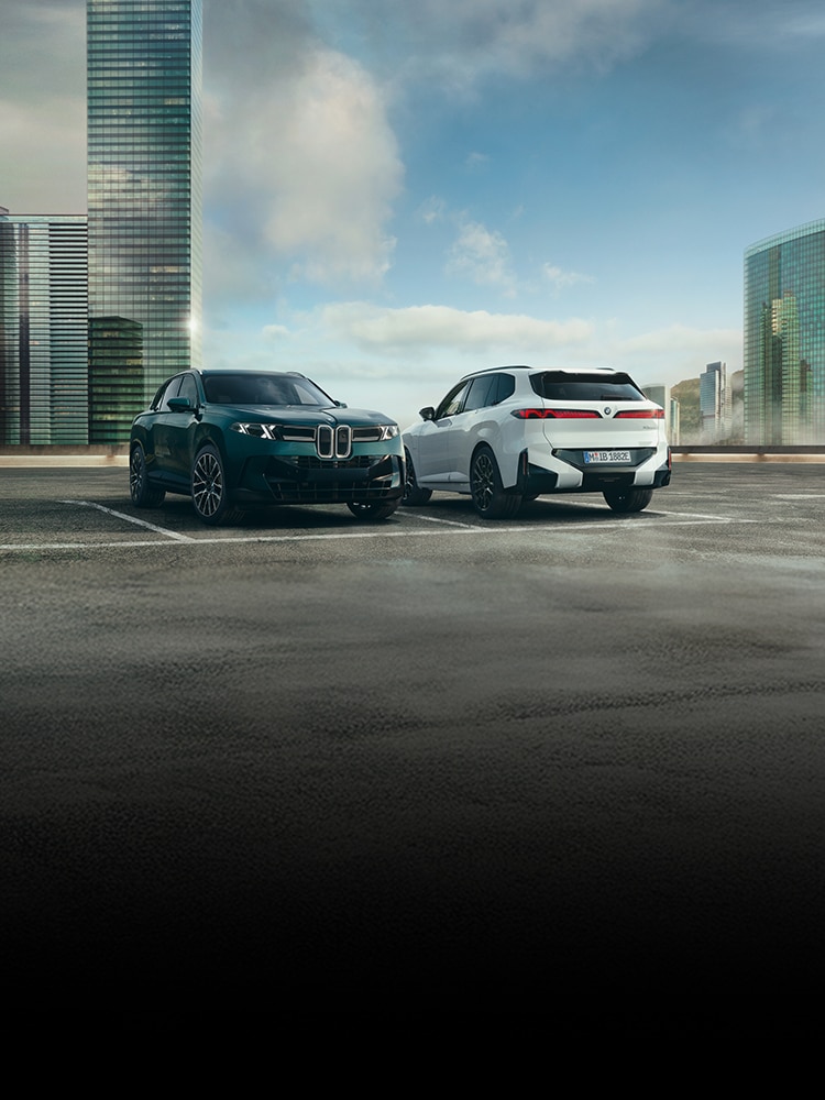 The BMW X5 40 xDrive and X5 50e xDrive sit parked on a rooftop parking lot amidst an urban environment.