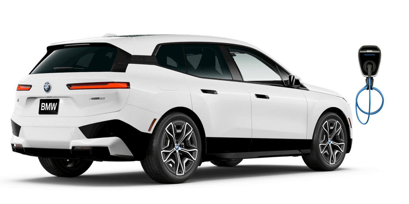 Angled rear view of BMW iX in Alpine White charging up with BMW Wallbox