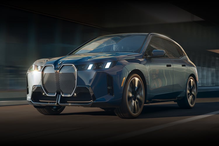 A three quarters shot of the front of the BMW iX as it races down an urban highway.