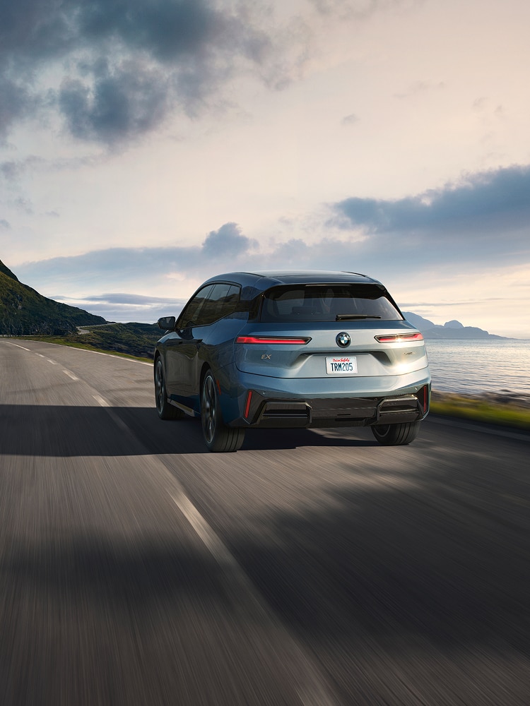 A rear shot of a BMW iX as it drives on a highway along a coastline