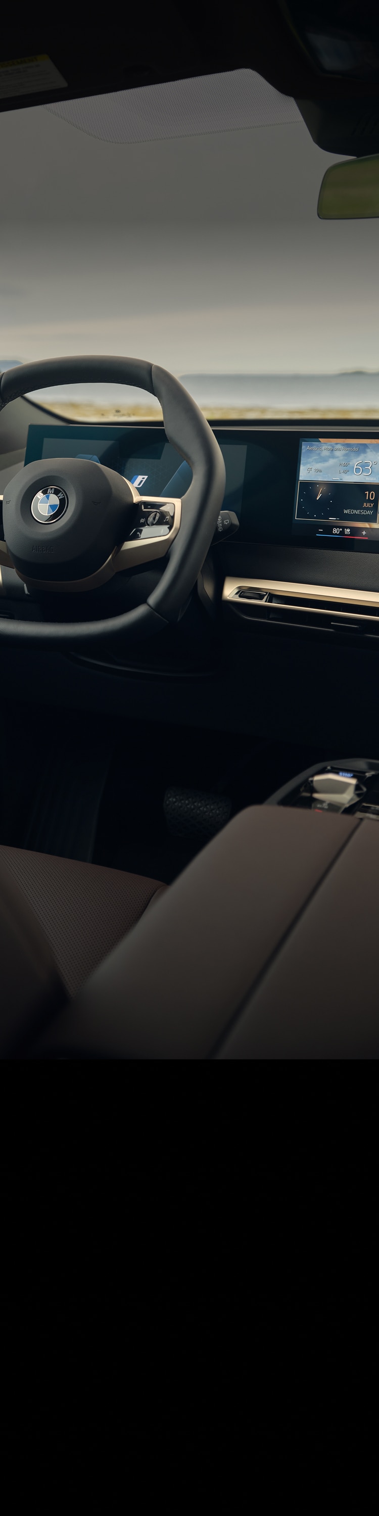 The cockpit of the BMW iX, including the steering wheel and the Curved Display showing weather and daily information