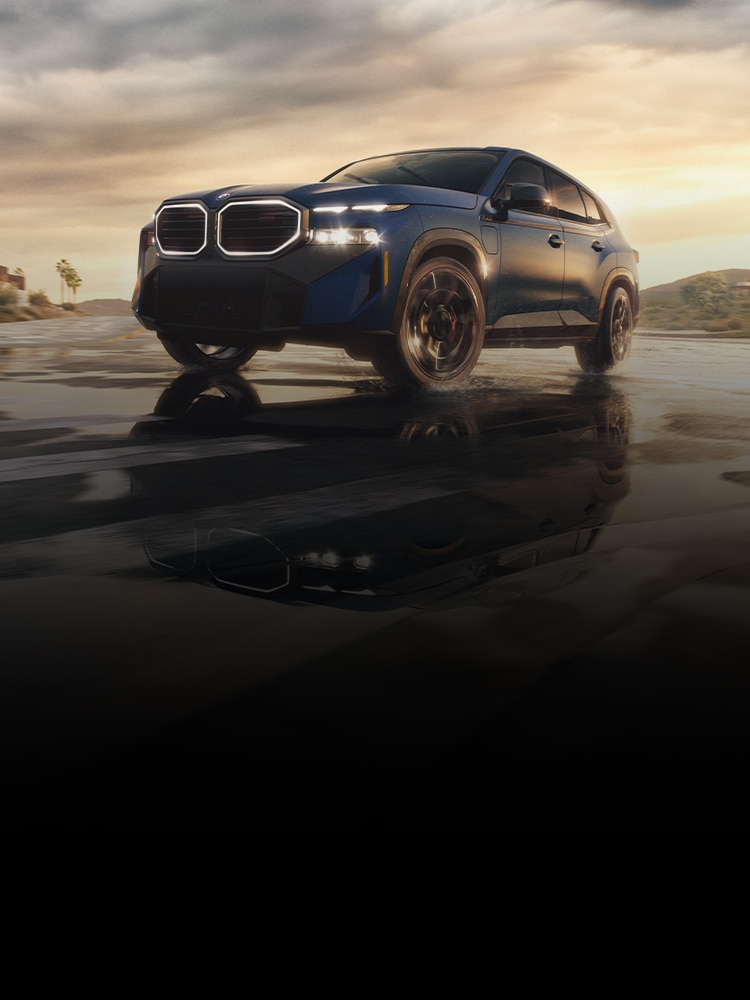 A profile view of the BMW XM Label in front of a sunset after a rainstorm, with a bold shadow reflecting from the pavement