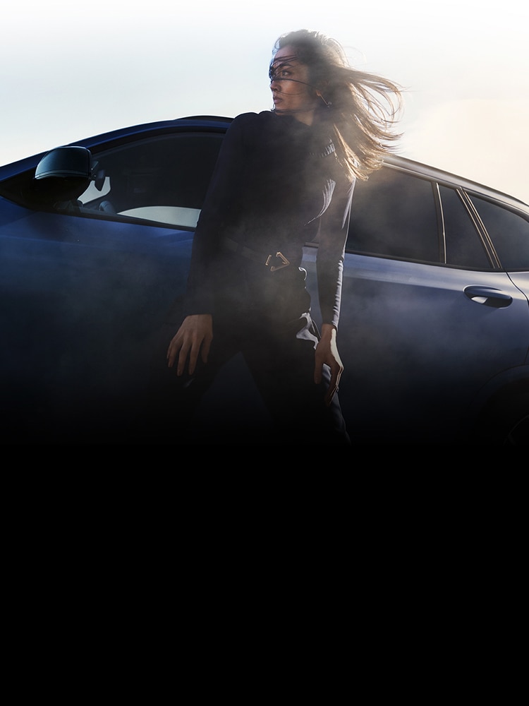 A woman stands outside her BMW X3 M with her hair blowing in the wind 