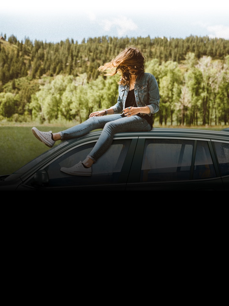 A woman sits on the roof of her parked BMW X3 with her hair blowing in the wind