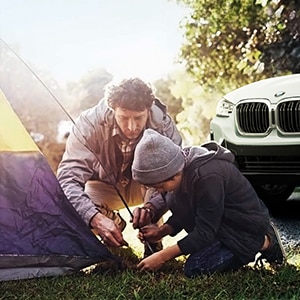 Father and child enjoy family time outdoors, setting up a small tent – with a BMW parked in the background