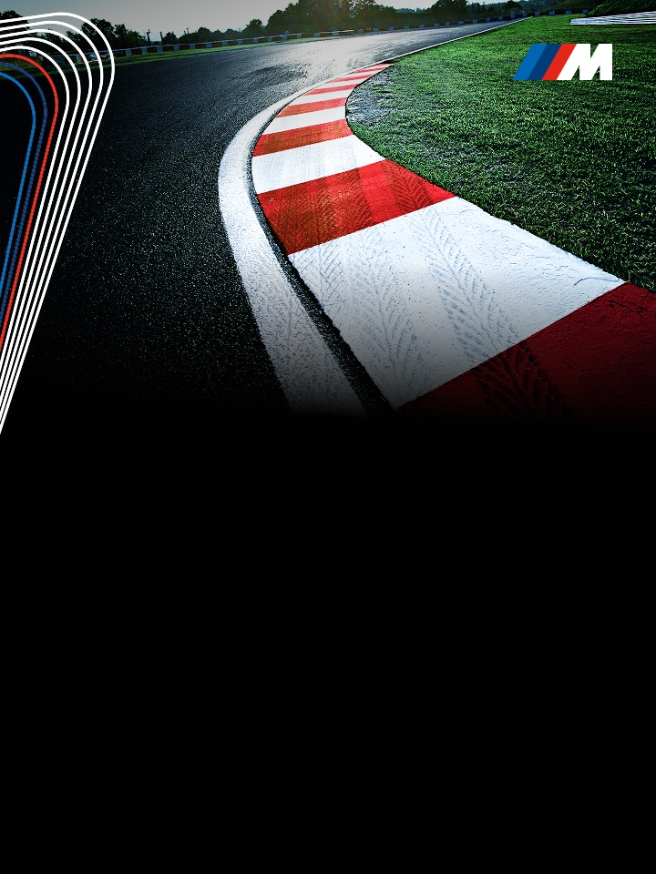 Close up of a racetrack, slightly slick with dew, with red and white striped curve hugging a tight corner of the track 